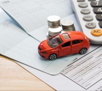 A miniature car on paper documents, coins, and a calculator, representing car insurance