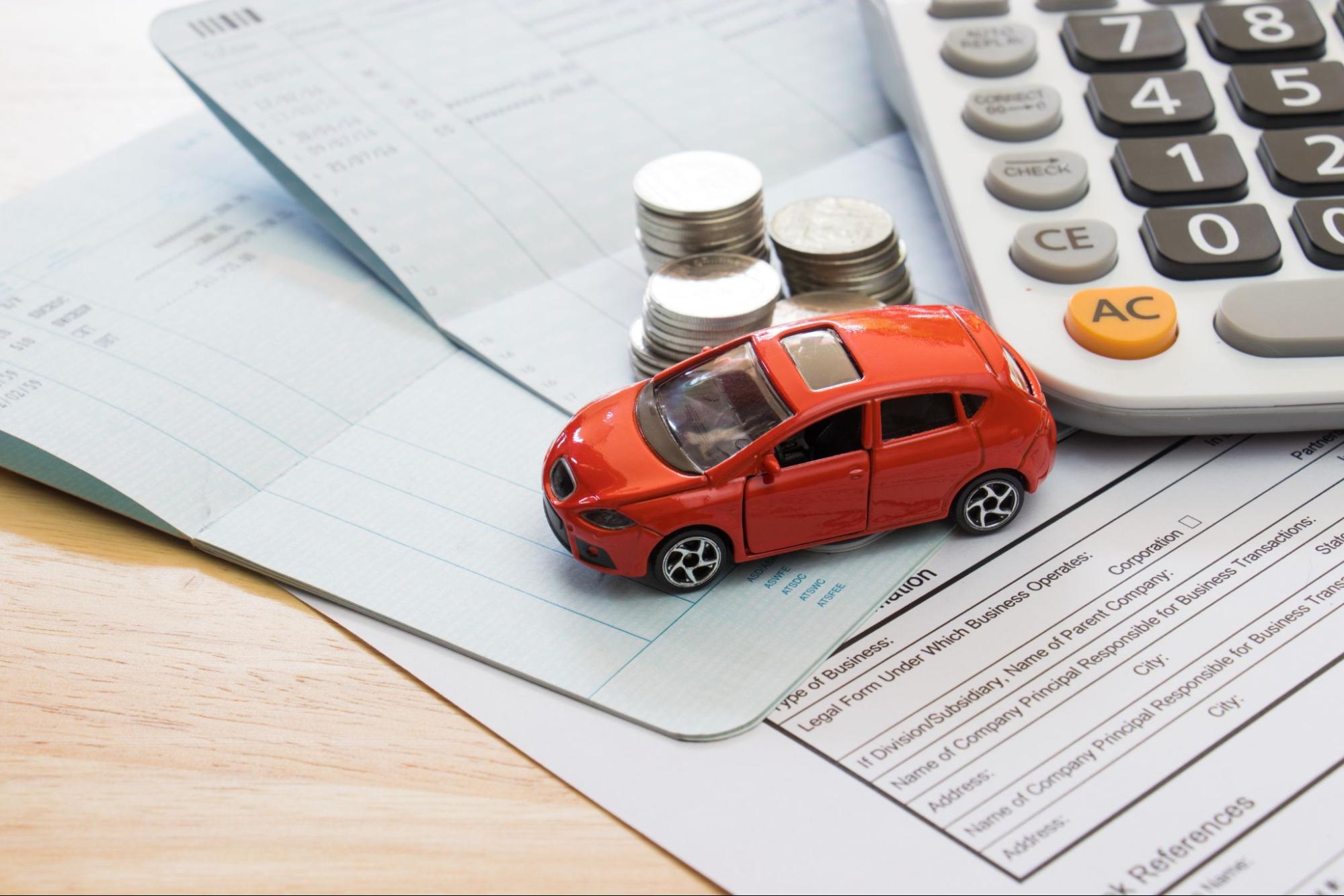 A miniature car on paper documents, coins, and a calculator, representing car insurance