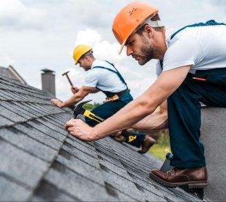 Two roofers on a roof, repairing the roof shingles