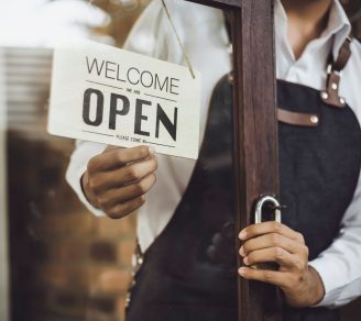 A cropped photo of a restaurant owner hanging the “open” sign