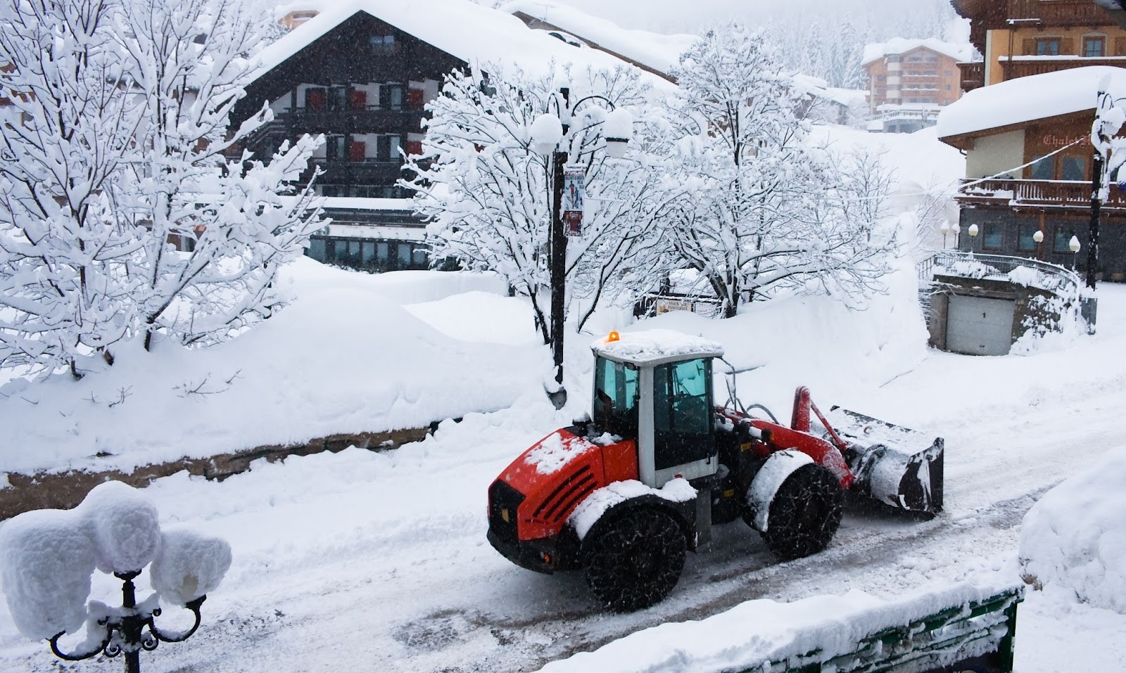 A red bulldozer clearing snow near a residential property