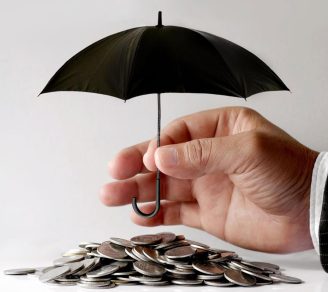 Close-up of a hand putting an umbrella over coins, representing what does umbrella liability insurance cover