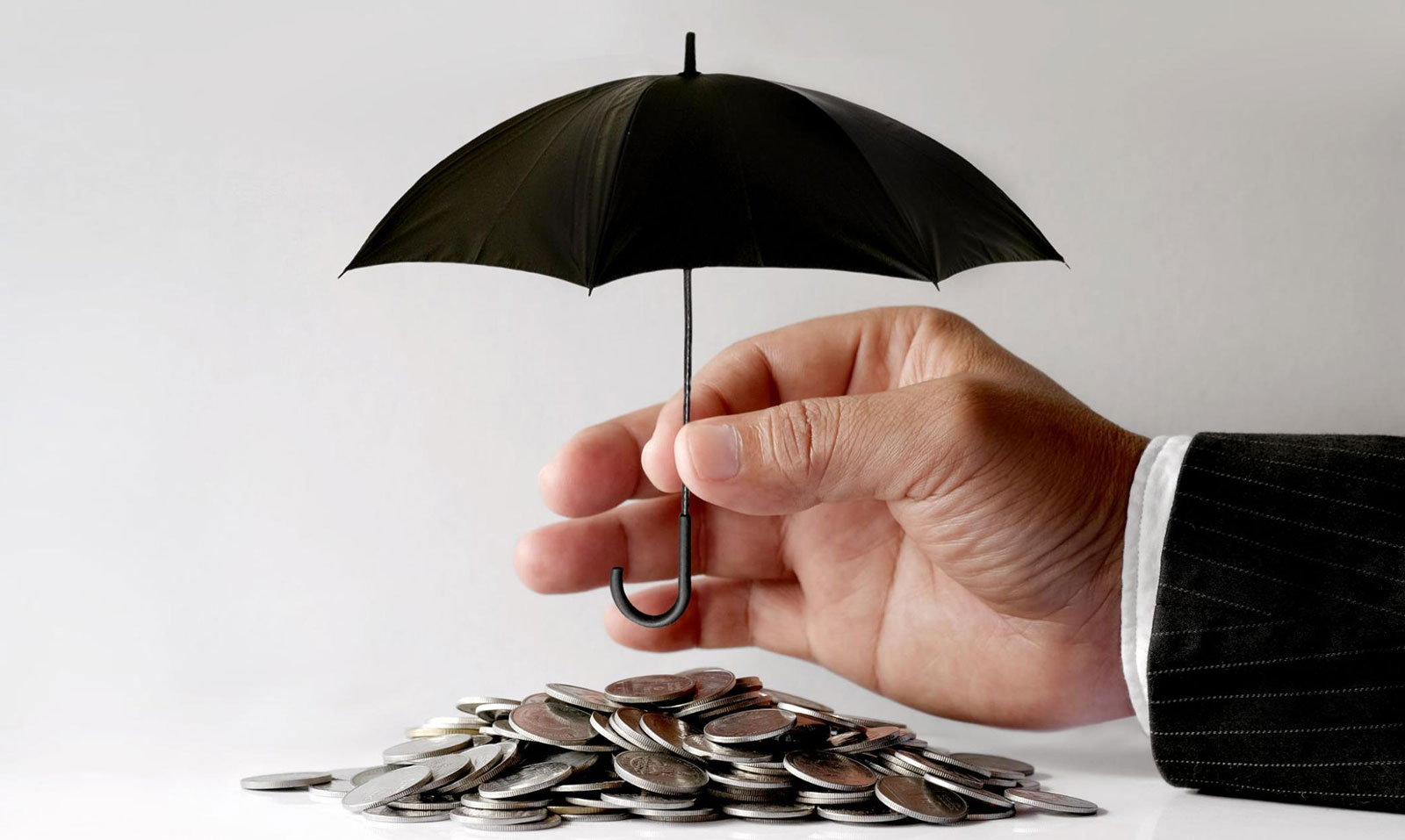Close-up of a hand putting an umbrella over coins, representing what does umbrella liability insurance cover