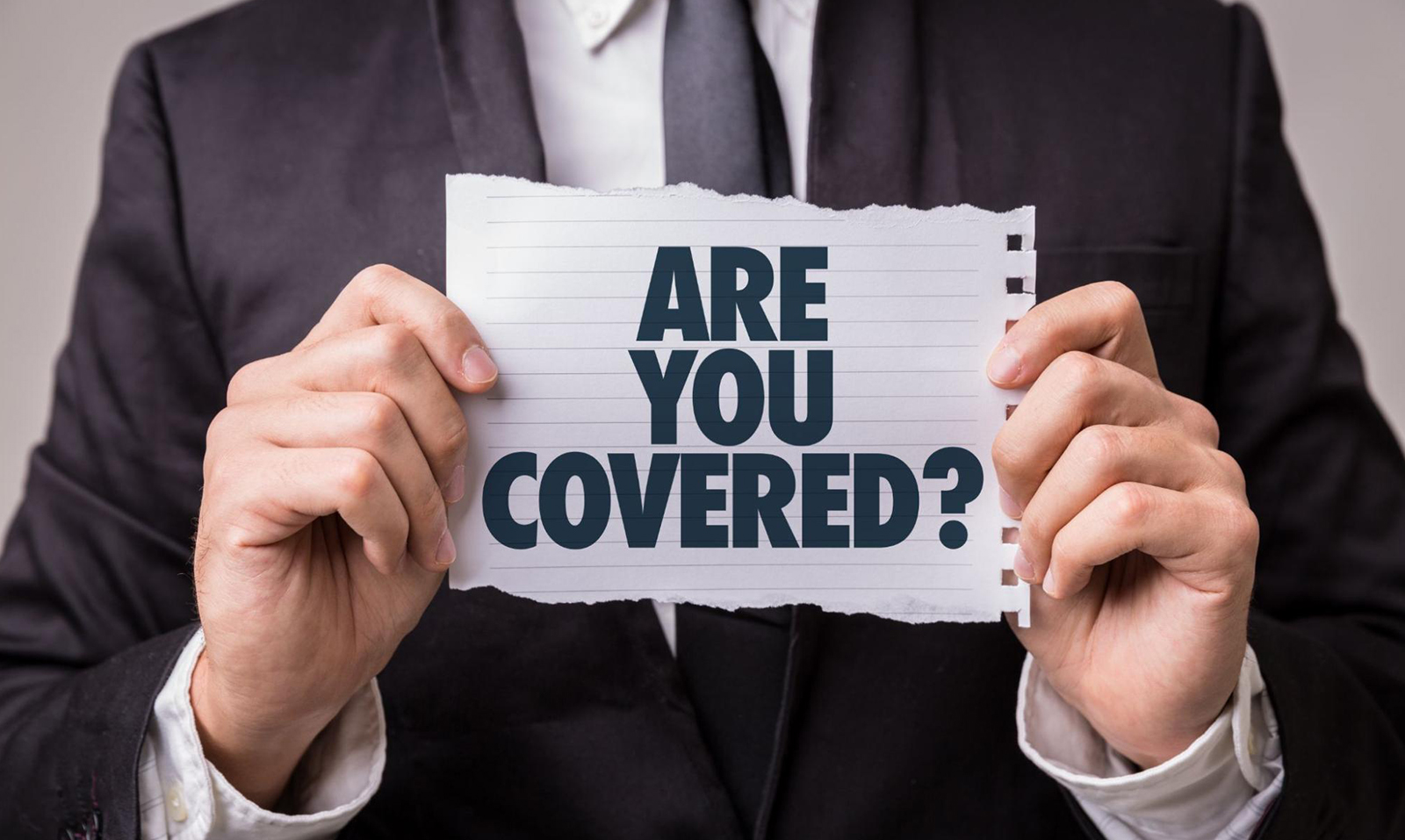 A man holding up a sign that says “Are You Covered?” suggesting the need for businesses to have CGL insurance