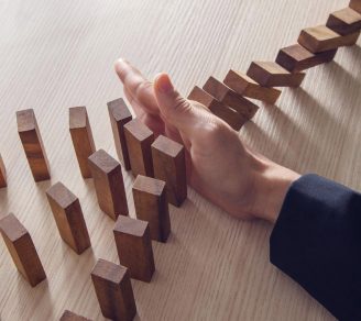 A hand stopping falling dominos representing how commercial risks need to be mitigated by commercial risk insurance