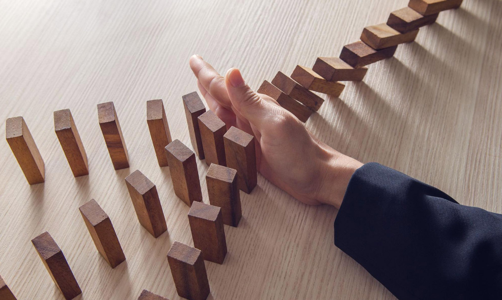 A hand stopping falling dominos representing how commercial risks need to be mitigated by commercial risk insurance