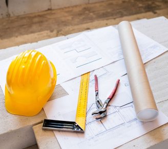 A hard hat, ruler, blueprints, and plier wrench on top of a table.