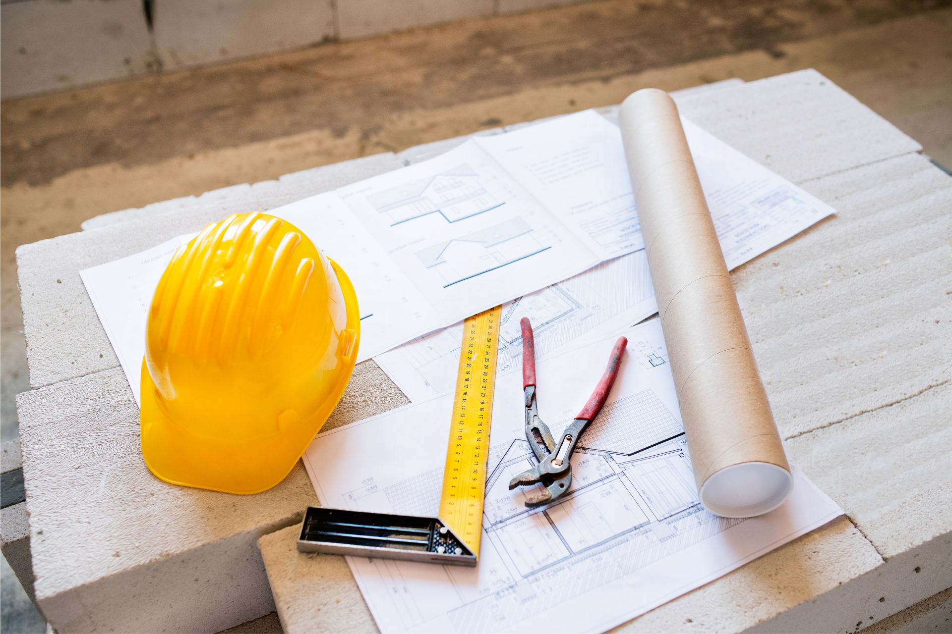 A hard hat, ruler, blueprints, and plier wrench on top of a table.