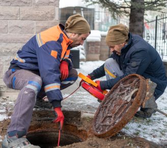 Two contractors in cold-weather gear fishing a line into a sewer