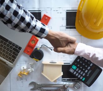 Two people shaking hands over documents and other construction materials