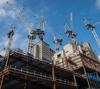 Several cranes surrounding a multi-story building under construction