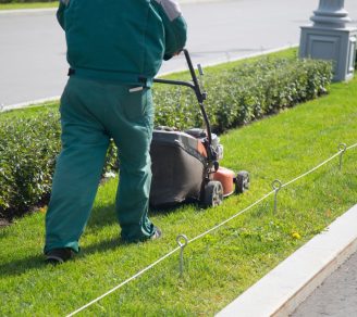 A landscape contractor mowing a narrow strip of grass