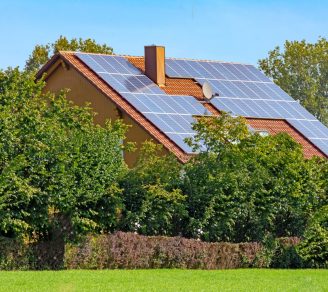A home surrounded by shrubbery with solar panels on the roof