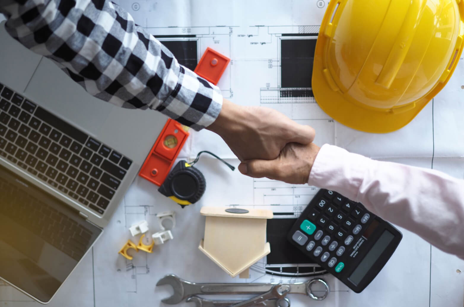 Two people shaking hands over documents and other construction materials