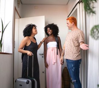 Airbnb host greeting two Airbnb guests with luggage at the front door