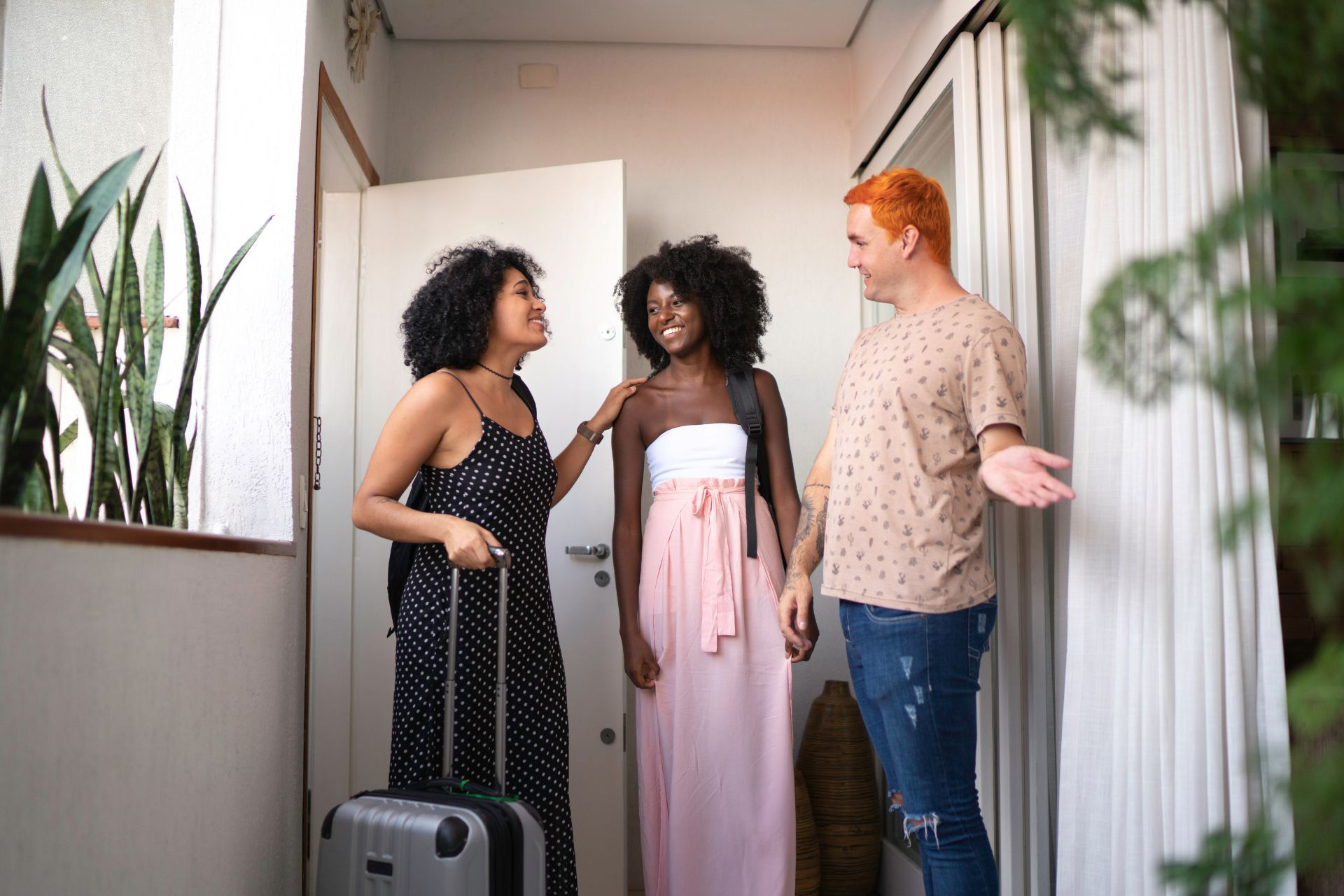 Airbnb host greeting two Airbnb guests with luggage at the front door