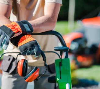 A landscape contractor holding hearing protection headphones while leaning on a mower